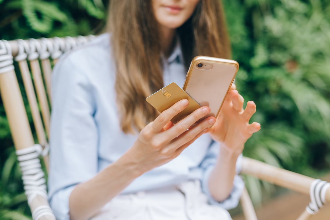 Contact A woman making an online purchase using a smartphone and credit card outdoors.