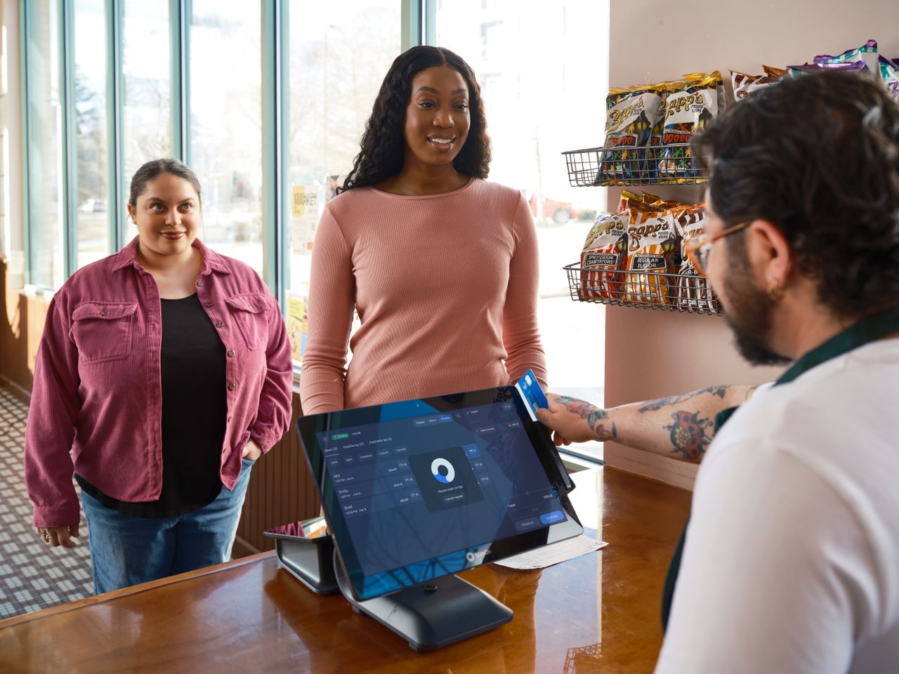 Home Two women making a payment at a convenience store using a touch screen POS system.